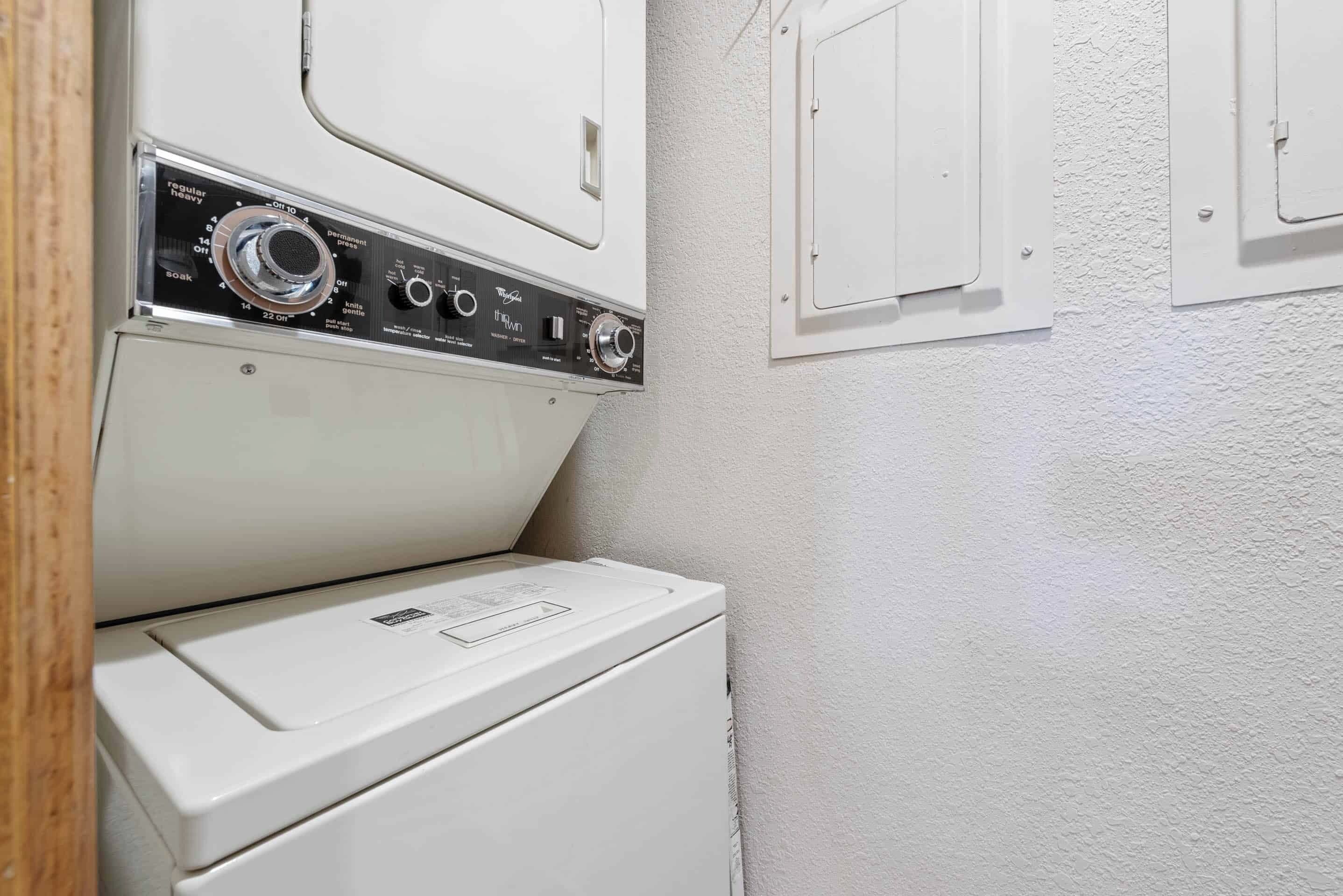 Une buanderie équipée d’un lave-linge et d’un sèche-linge à chargement frontal, d’un panneau de commande et d’un mur blanc avec une porte.