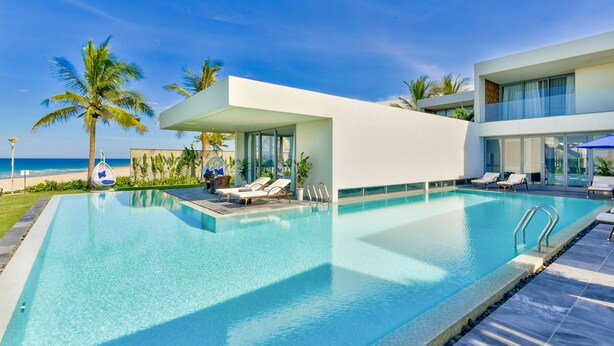 A modern pool area with lounge chairs, a glass-enclosed structure, and a view of the ocean. - Abogo Da Nang OceanFront Luxury Villa (Da Nang)