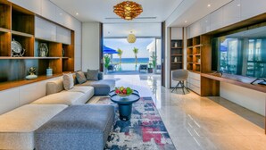 A modern living room with a sofa, coffee table, and shelves. There is a view of the ocean through large windows. - Abogo Da Nang OceanFront Luxury Villa (Da Nang)
