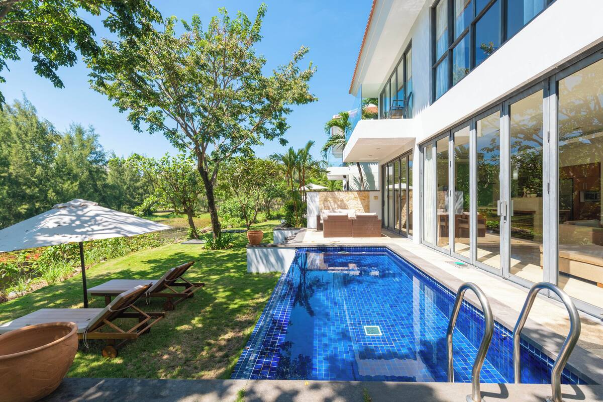 Una piscina con suelo de baldosas, sillas de descanso y una pérgola con sombrilla.