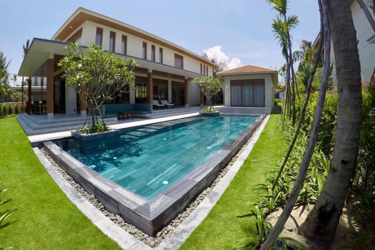 Una casa moderna con piscina, un porche cubierto y un jardín con palmeras.