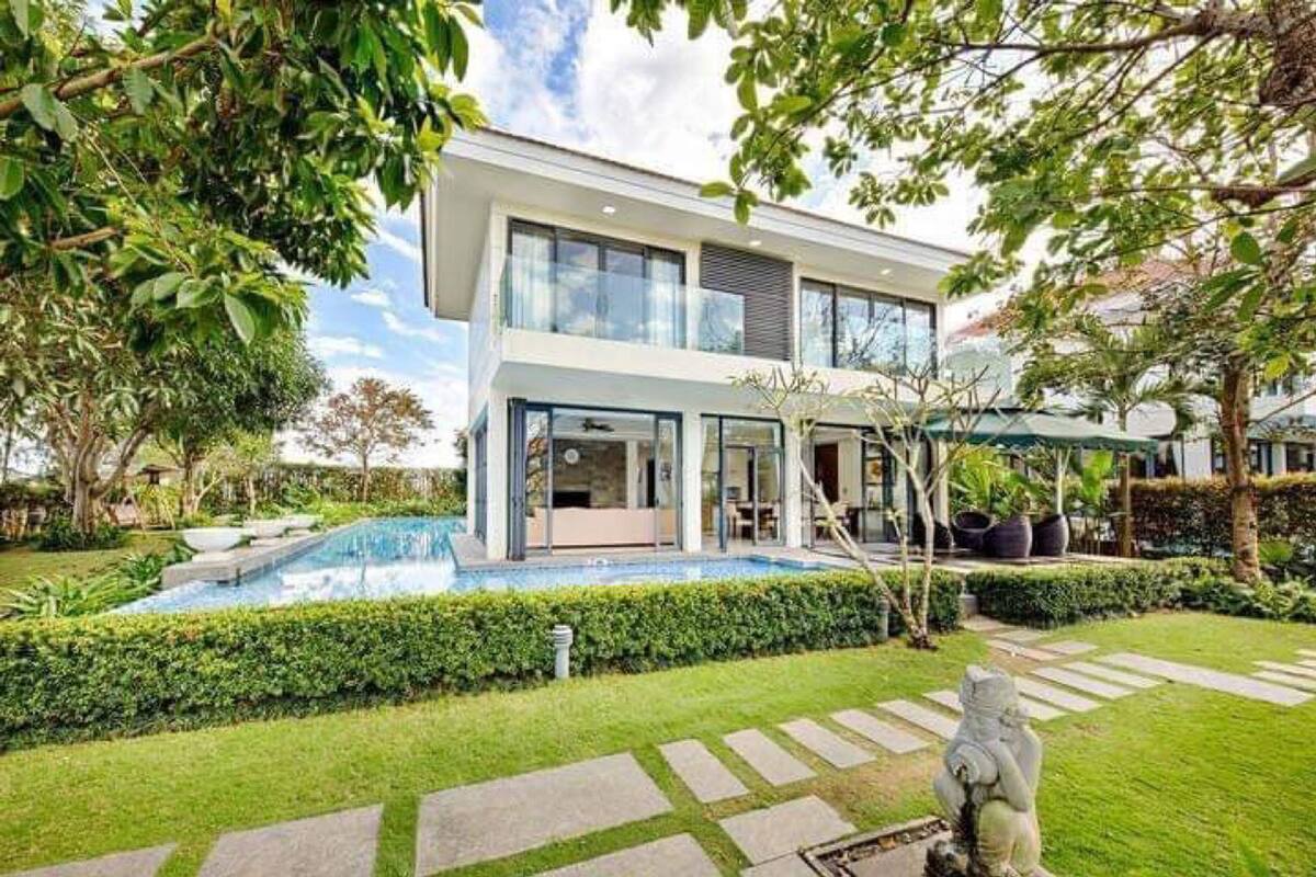Una casa moderna de dos pisos con piscina, rodeada por un jardín cuidado y un camino de piedra.