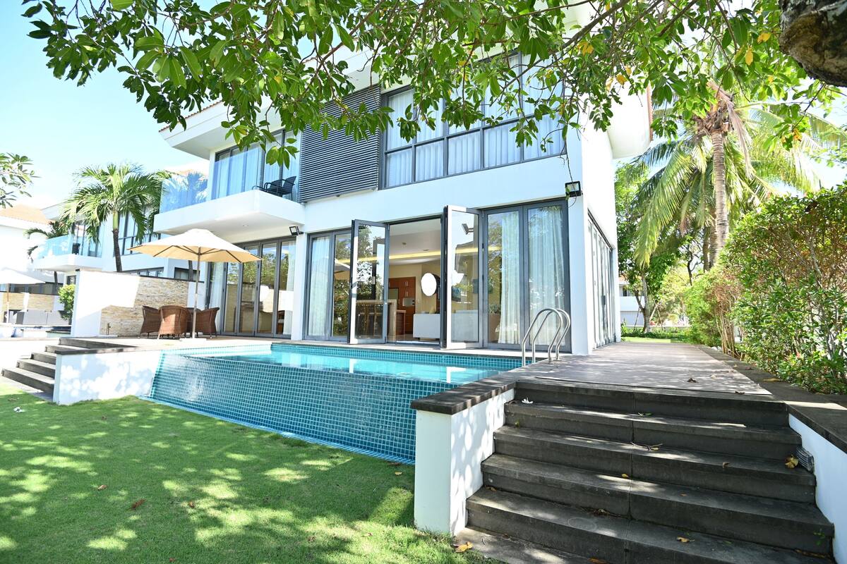 Una casa moderna con piscina, una escalera que lleva a la entrada y un patio con mobiliario exterior.