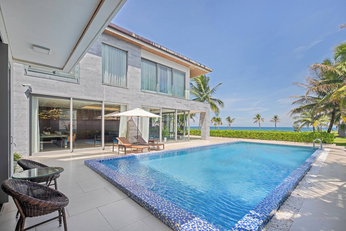Una casa moderna con piscina, mobiliario exterior y vistas al océano.