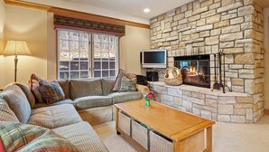 A cozy living room with a stone fireplace, a comfortable sectional sofa, a wooden coffee table, and a television mounted on the wall. - The Charter at Beaver Creek G0505 (Beaver Creek)