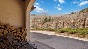 Eine Terrasse mit Stühlen und einem Holzstapel, mit Blick auf eine Steinmauer und eine angelegte Grünfläche mit Bäumen und Sträuchern.