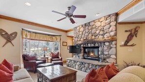 A cozy living room with a stone fireplace, leather furniture, and a ceiling fan. - The Charter at Beaver Creek F3505 (Beaver Creek)