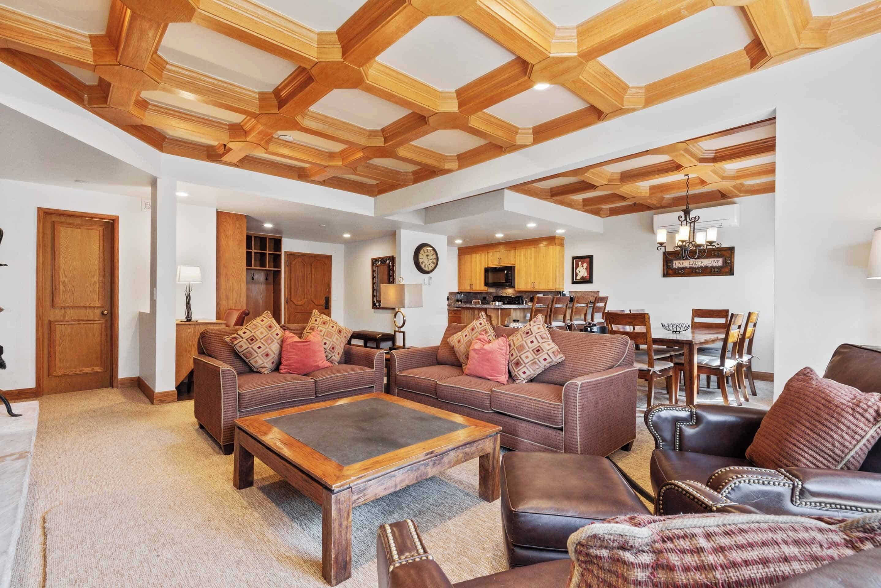 Ein geräumiges Wohnzimmer mit Holzbalken, einem Essbereich mit einer Kronleuchter und einer Küche mit Holzschränken.