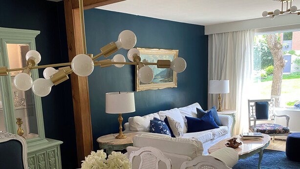 Un comedor con una mesa dispuesta para cuatro personas, un jarrón de flores y una pared azul con un cuadro enmarcado.