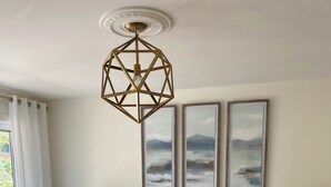 Un dormitorio con una cama grande, dos mesitas de noche con lámparas, una lámpara de techo geométrica y tres pinturas de paisajes en la pared.