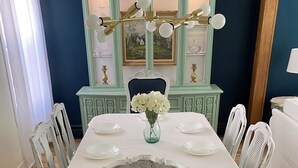 Comedor con una mesa blanca dispuesta para cuatro, un jarrón de flores blancas y un mueble azul aguamarina con puertas de cristal.