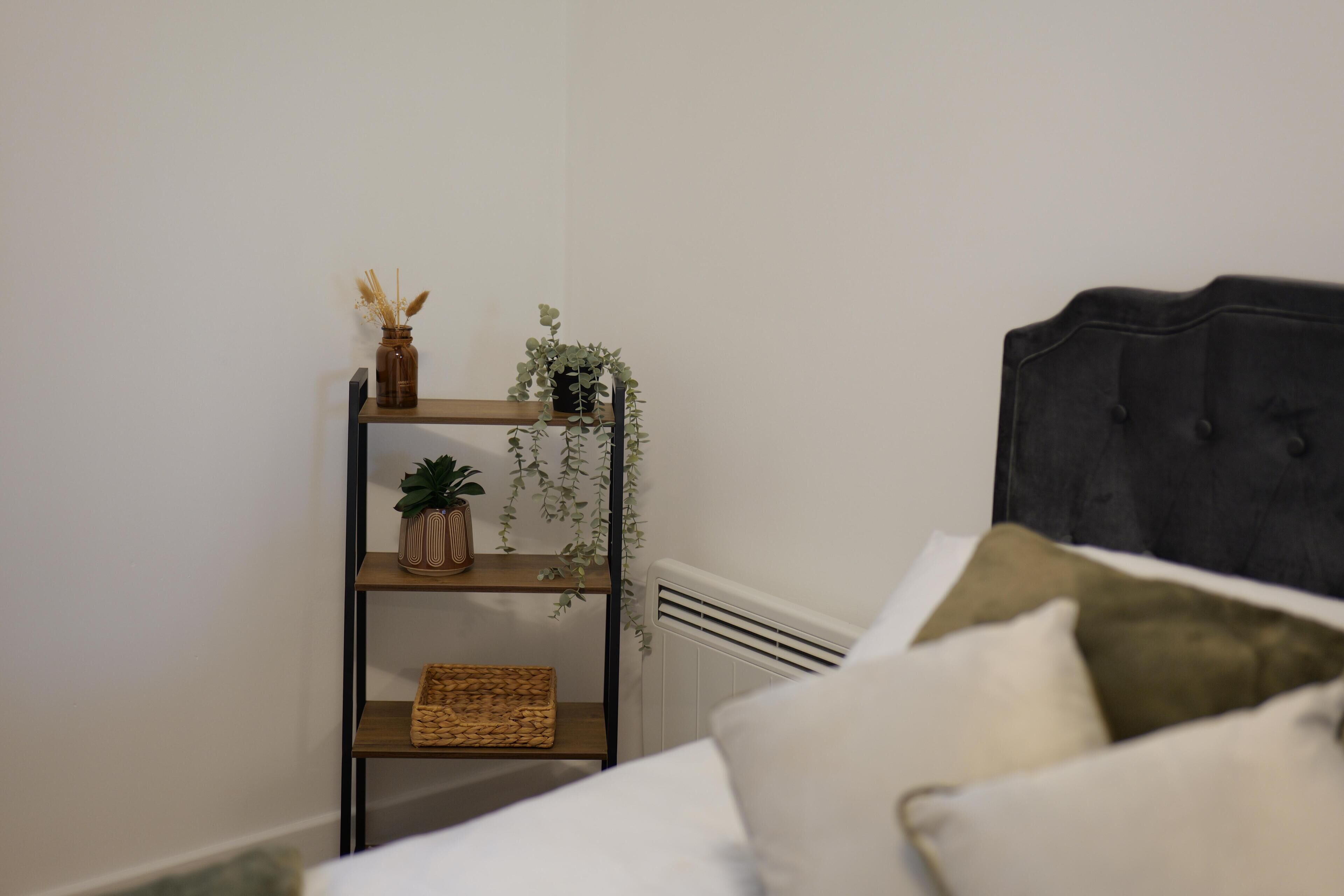 A bedroom with a bed, a bedside table with a plant, and a radiator.