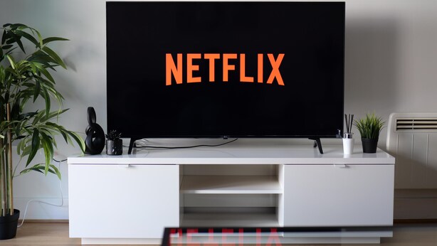 Ein Flachbildfernseher auf einer weißen Unterhaltungsecke, auf dem das Wort 'NETFLIX' angezeigt wird.