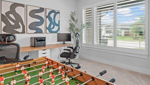A room with a foosball table, a desk with a computer, a chair, and artwork on the wall. - Close to CotA & Downtown | Spacious & Luxe | 4BR (Austin)
