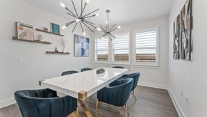 A modern dining area with a white table, dark blue chairs, and a unique chandelier. - Close to CotA & Downtown | Spacious & Luxe | 4BR (Austin)