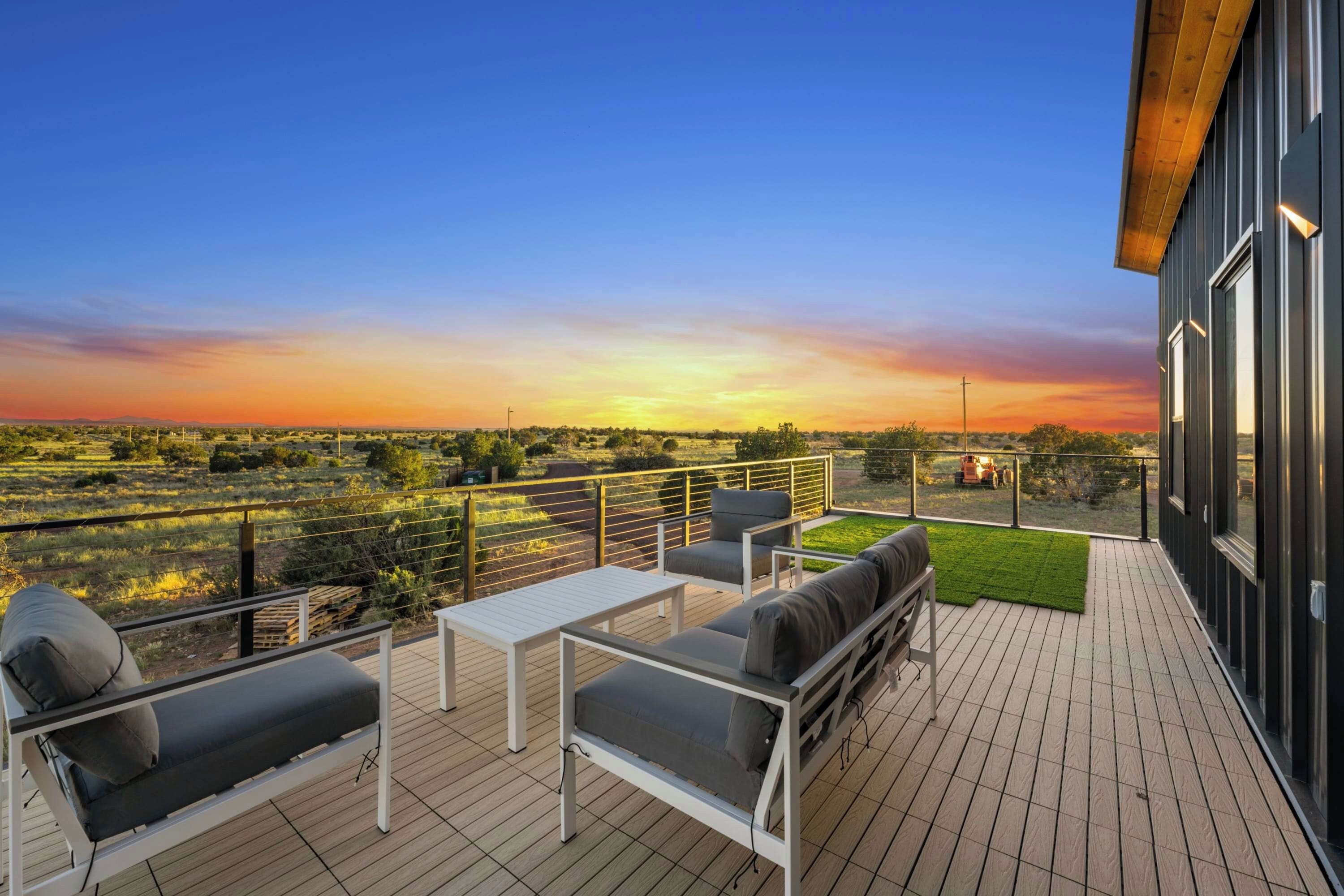 A deck with outdoor furniture, a view of the countryside, and a sunset.