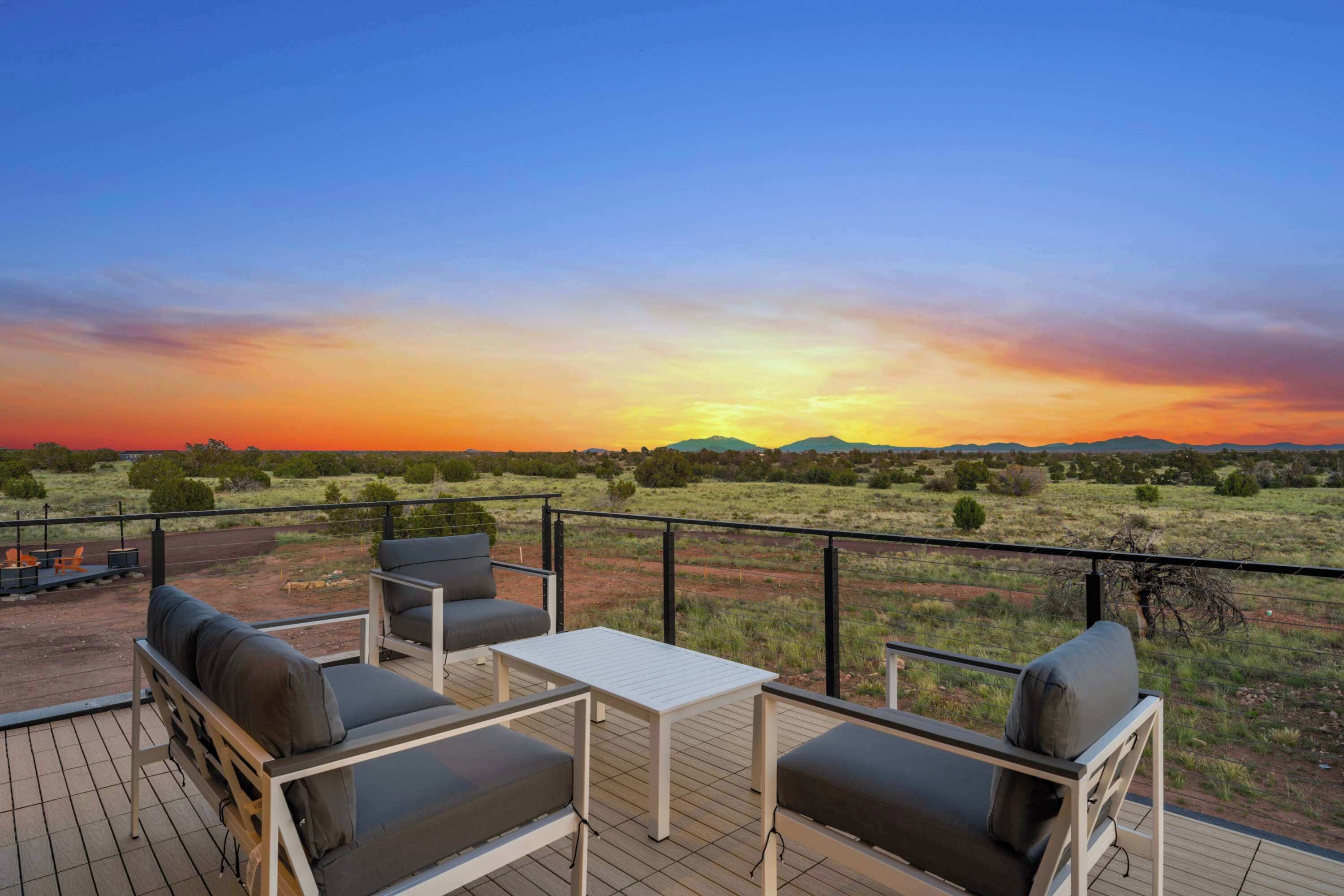 Una terraza con mobiliario exterior y vista a la puesta de sol sobre un paisaje llano.