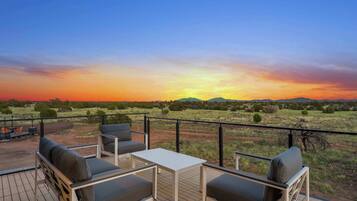 Una terraza con mobiliario exterior y vista a la puesta de sol sobre un paisaje llano.