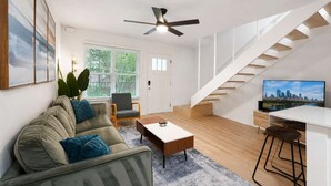 A modern living room with a sofa, coffee table, and TV. There's a staircase with a city view.