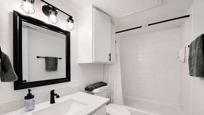 A modern bathroom with a white sink, black faucet, and a mirror with three lights.