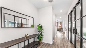 A hallway with a dark wooden console table, a potted plant, and a large mirror on the wall. - Close to CotA & Downtown | Cozy & Luxe | 4BR (Austin)