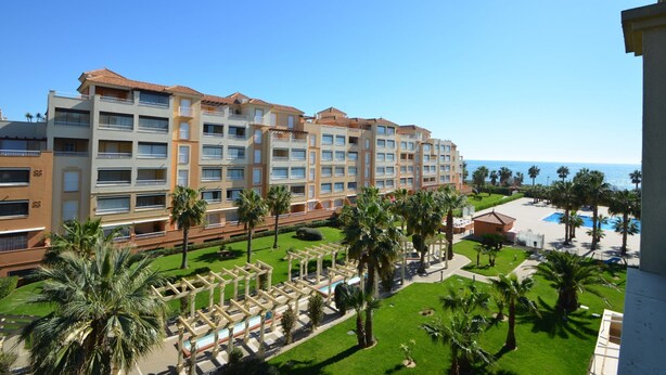 Un hotel de varios pisos con balcones, zona de piscina y palmeras.