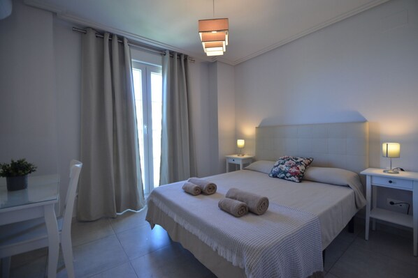 A hotel room with a bed, two bedside tables, a desk, a chair, and a window with curtains.
