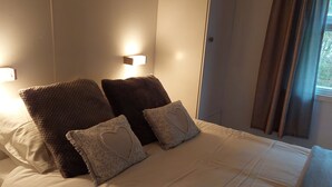 Un letto ben rifatto con una coperta bianca e due cuscini decorativi, uno con un motivo a cuore.