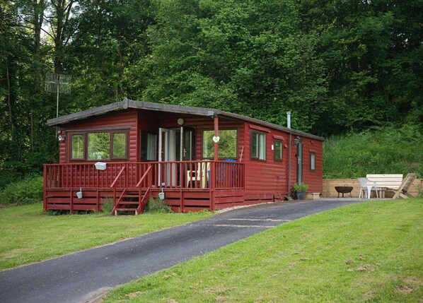 En liten, enplansstuga med en veranda, en gångstig som leder fram till den och en bänk i närheten.