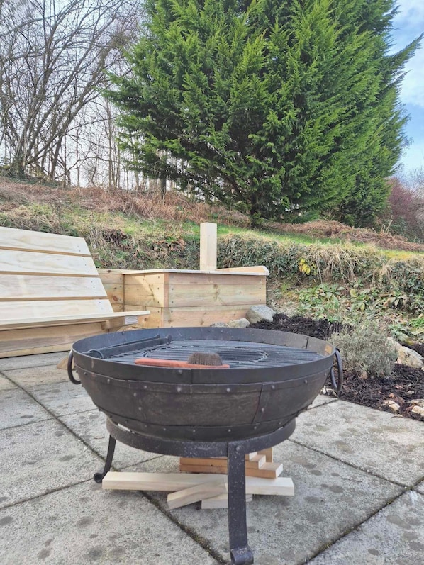 A portable outdoor grill on a concrete patio with wooden planks and a tree in the background. - Number 8 Lodge Caer Beris (Builth Wells)