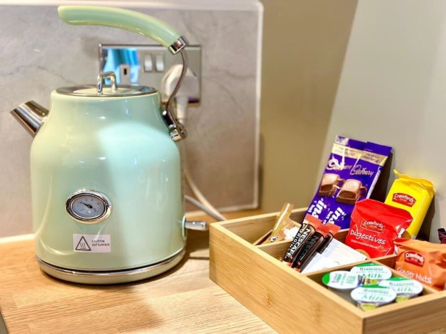 Een keuken met een lichtblauwe waterkoker, een houten doos met verschillende etenswaren, en een marmeren spatwand.