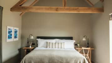 A bedroom with a large bed, wooden beams, a hanging light fixture, a bedside table with a lamp, and a bench.