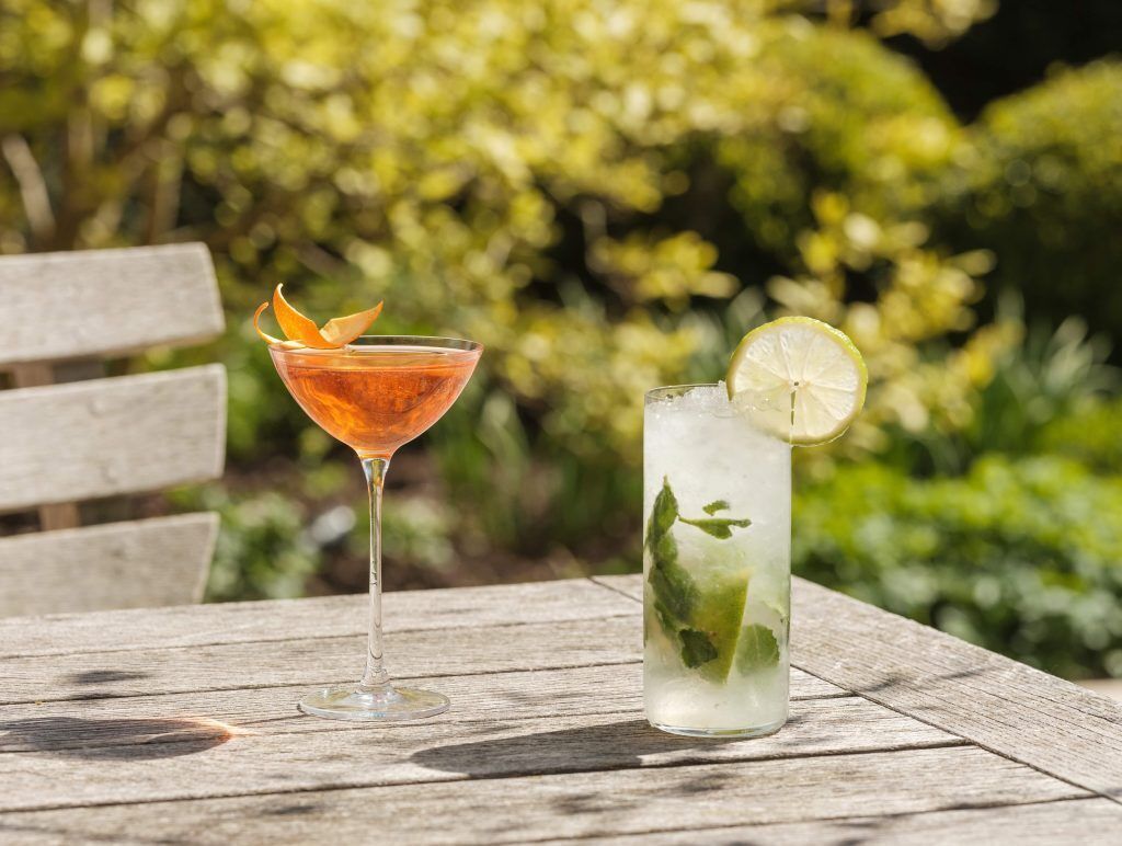 Dos bebidas sobre una mesa de madera al aire libre, con follaje de fondo.