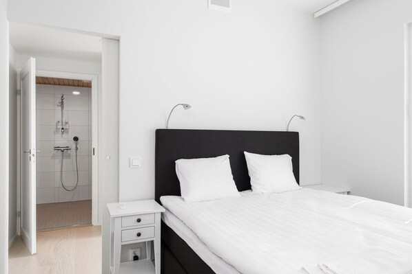 A modern bedroom with a large bed, bedside tables, and a walk-in shower. - Borg Housing Katariinankatu (Pori)