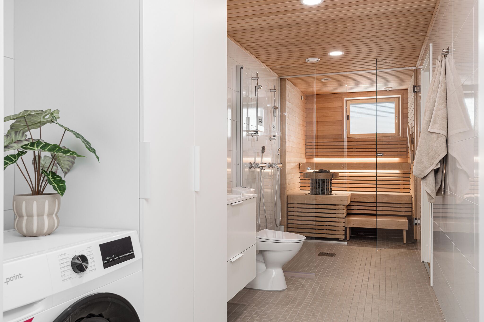 A modern bathroom with a glass shower enclosure, a wooden bench, and a potted plant.