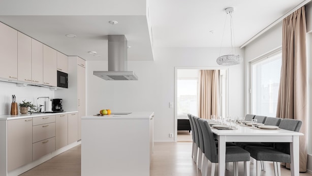 A modern kitchen with a central island, white cabinetry, and a dining area with a white table and grey chairs.