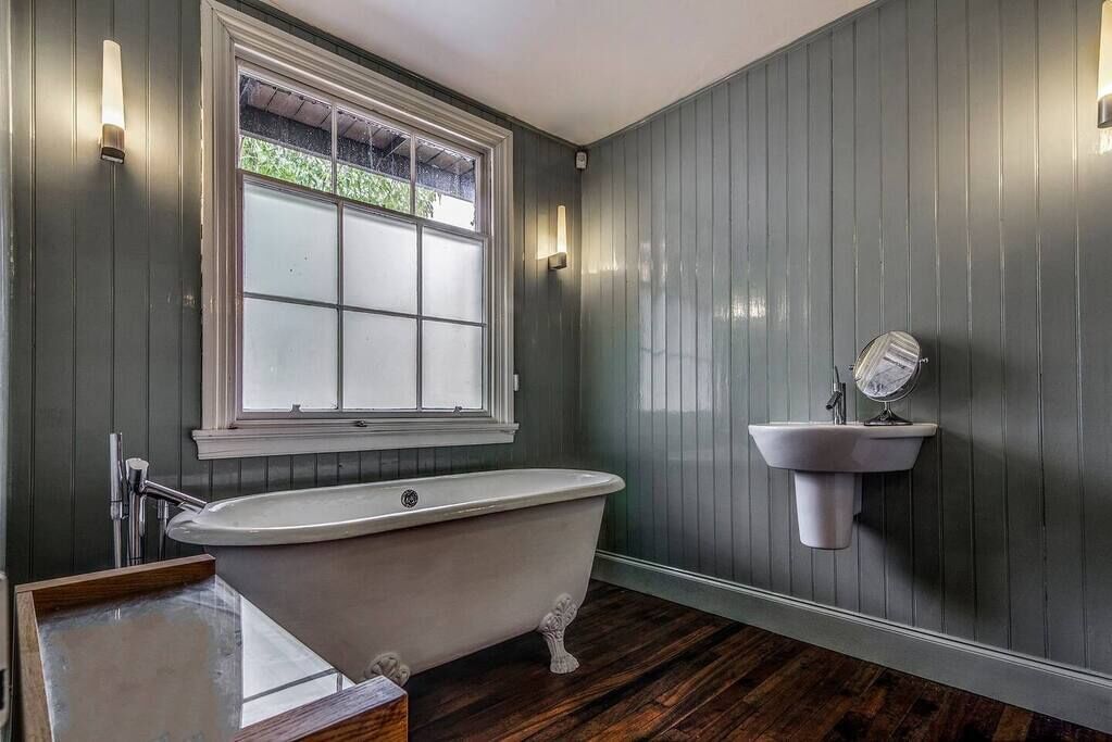 Une salle de bain avec une baignoire sur pieds, une fenêtre à verre dépoli et un lavabo fixé au mur.