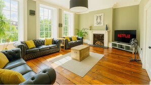 Ein Wohnzimmer mit Kamin, einer Sofagarnitur, einem Couchtisch und einem Fernseher, der 'NETFLIX' zeigt.