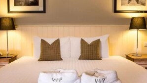 A hotel room with a large bed, two pillows, two bedside lamps, and two towels with "VIP" on them.