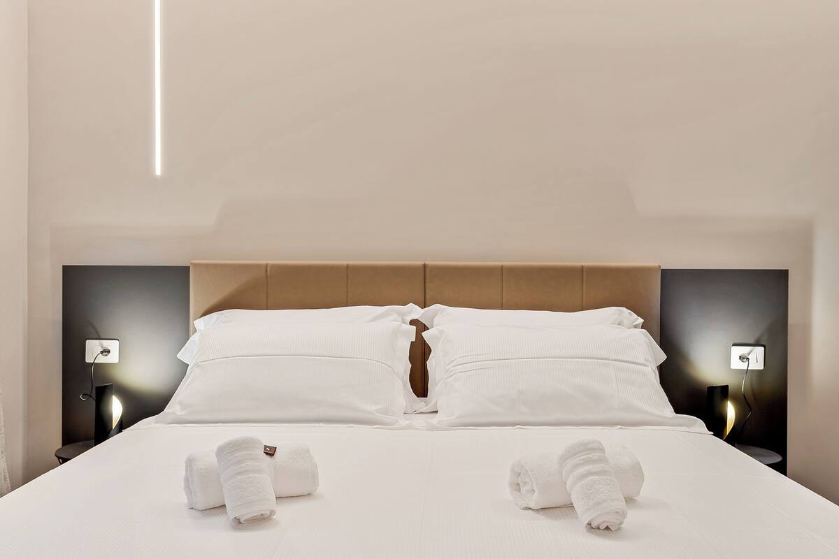 Ein ordentlich bezogenes Bett mit weißen Leinen und Handtüchern, ein hölzerner Kopfteil sowie Nachttischlampen.