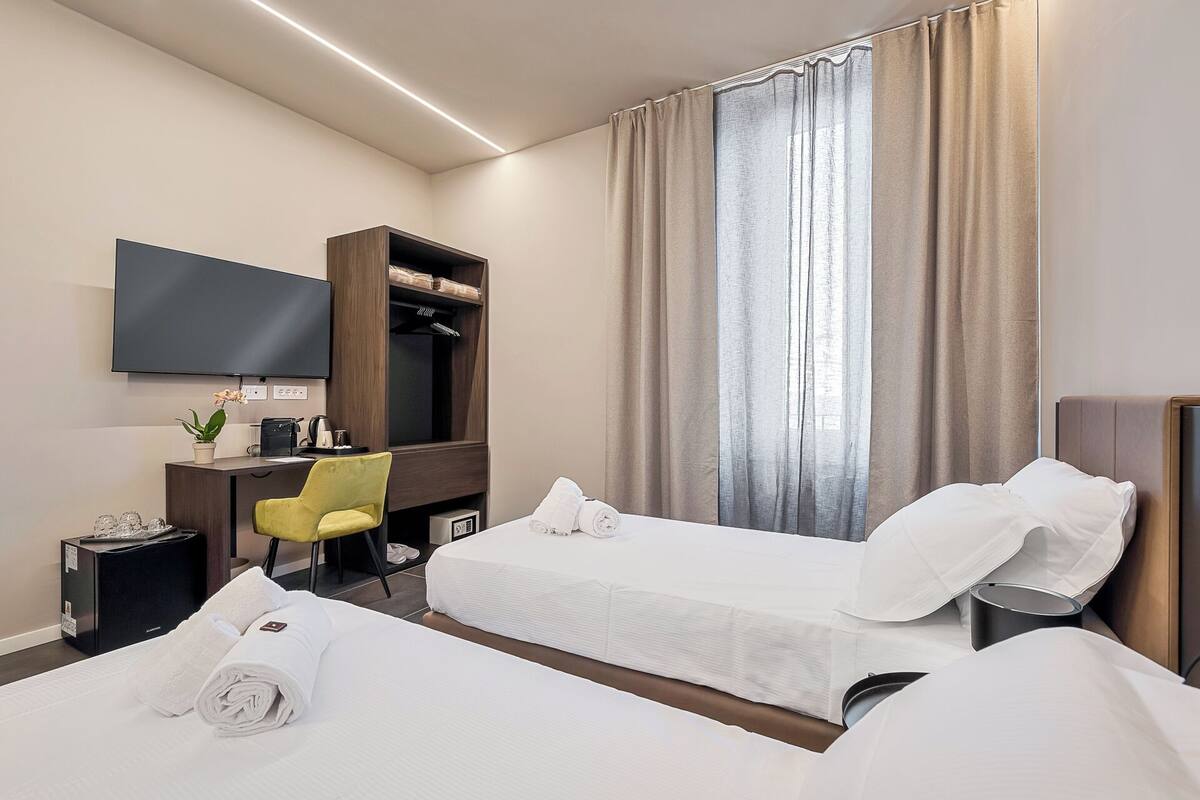 Ein Hotelzimmer mit zwei Betten, einem Schreibtisch mit Stuhl, einem Fernseher und einem Kleiderschrank.
