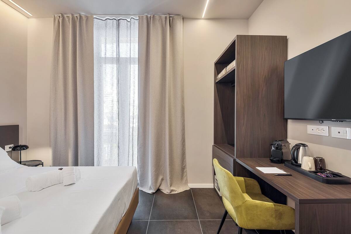 Ein Hotelzimmer mit Bett, Schreibtisch, Stuhl, Fernseher und Kleiderschrank.