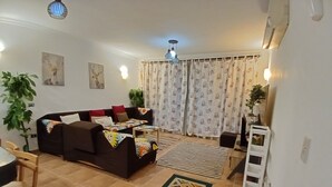 Ein Wohnzimmer mit einer Couch, einem Couchtisch, einem gemusterten Teppich und einem Essbereich mit einem Stuhl und Tisch.