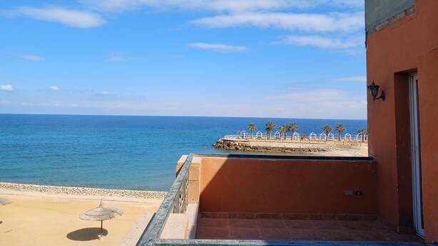 Ein Balkon mit Blick auf das Meer, ein Sandstrand und ein Gebäude mit einer Tür und einer Wandleuchte.