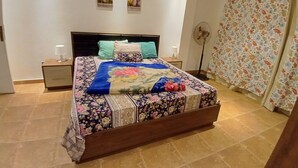 Ein Schlafzimmer mit einem Bett, Nachttischen, einem Ventilator und einem Fenster mit floralem Vorhang.