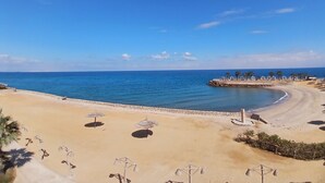 Ein Strand mit Sonnenschirmen und einem Felsen mit Palmen.