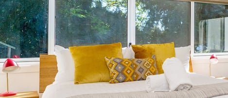 Relax in a serene space with a large bed, two bedside tables, and a large window offering a view of lush greenery.