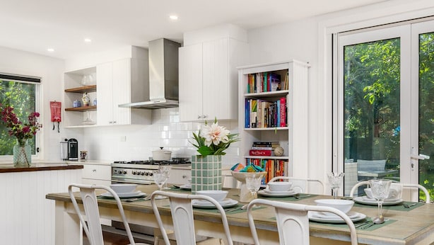 A modern kitchen with white cabinetry, a dining table set for four, and a bookshelf filled with books. - Garden Precinct 3BR, Walking distance to Airport (Pialligo)