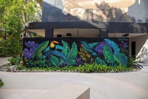 A mural of tropical leaves and birds on a building's exterior wall. - Safe & Beautiful Studio: Parking, Padel & Pool (Tulum)