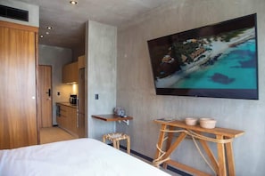 A hotel room with a bed, a wooden desk, a television mounted on the wall, and a small kitchen area. - Safe & Beautiful Studio: Parking, Padel & Pool (Tulum)